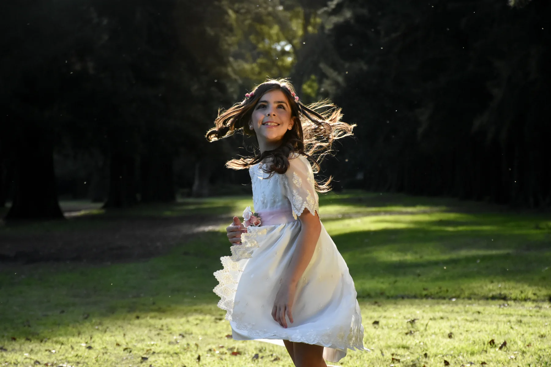 Nena con vestido blanco girando en un parque a contraluz